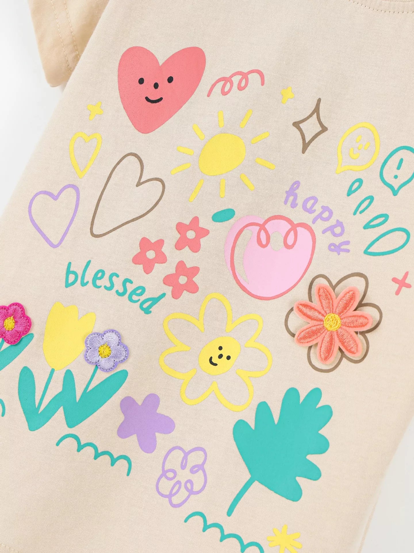 Apricot kids T-shirt with hearts, sun, happy lettering and embroidered flower accents, graphic close-up