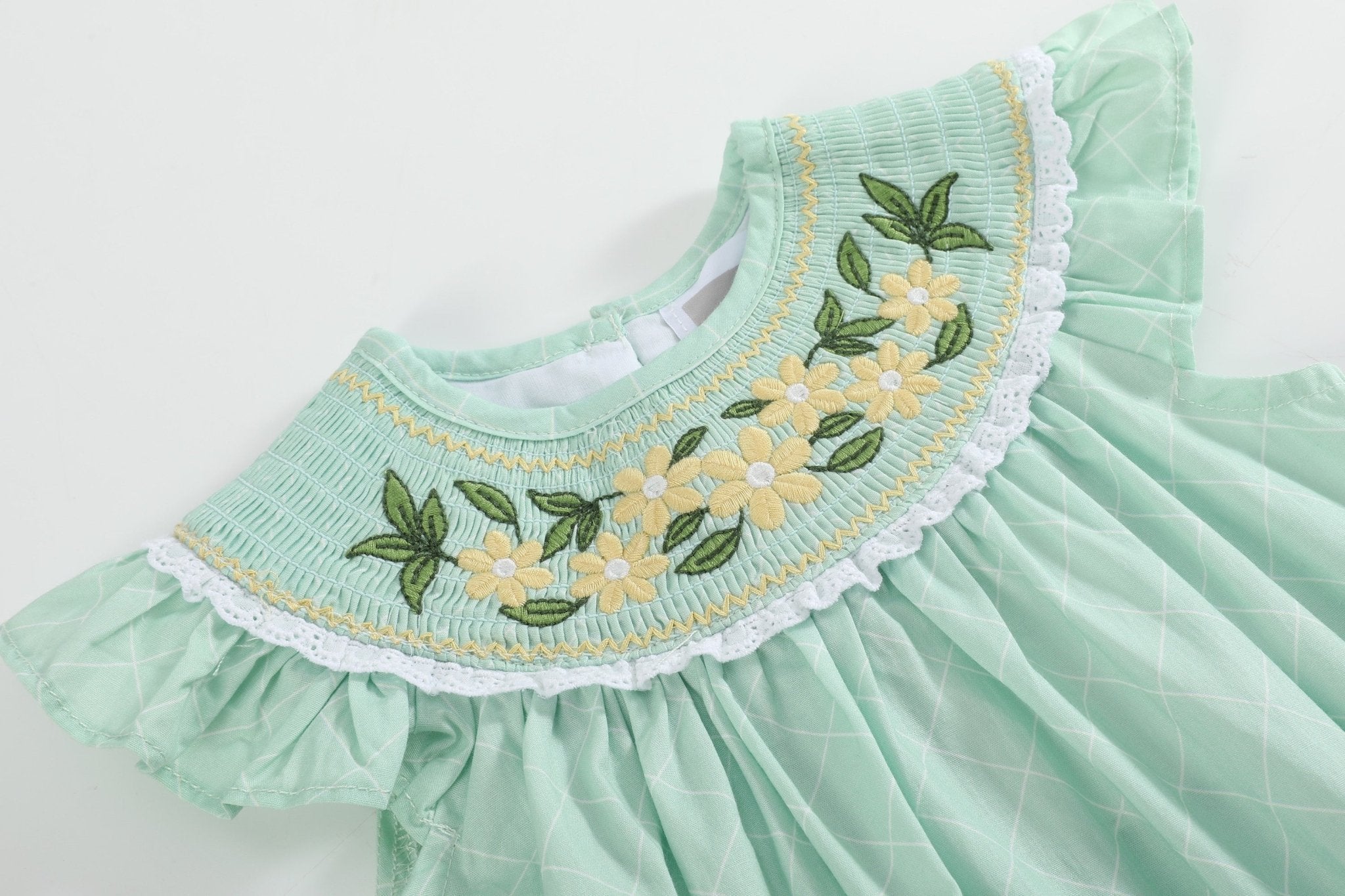 Aqua baby romper with yellow daisy embroidery and white lace-trimmed smocked yoke, close-up view