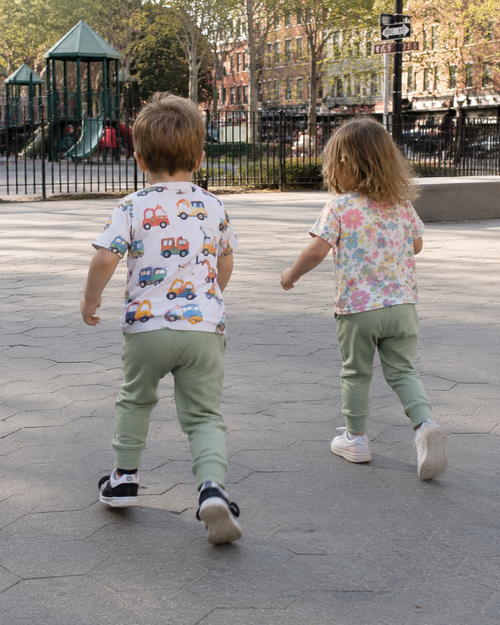 Army green kids jogger pants worn by two children, rear playground lifestyle view
