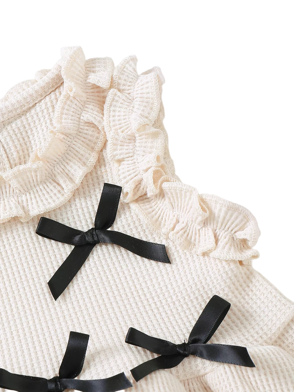 Ivory baby waffle knit top with black satin bows and layered ruffle shoulder trim, bodice close-up