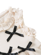 Ivory baby waffle knit top with black satin bows and layered ruffle shoulder trim, bodice close-up