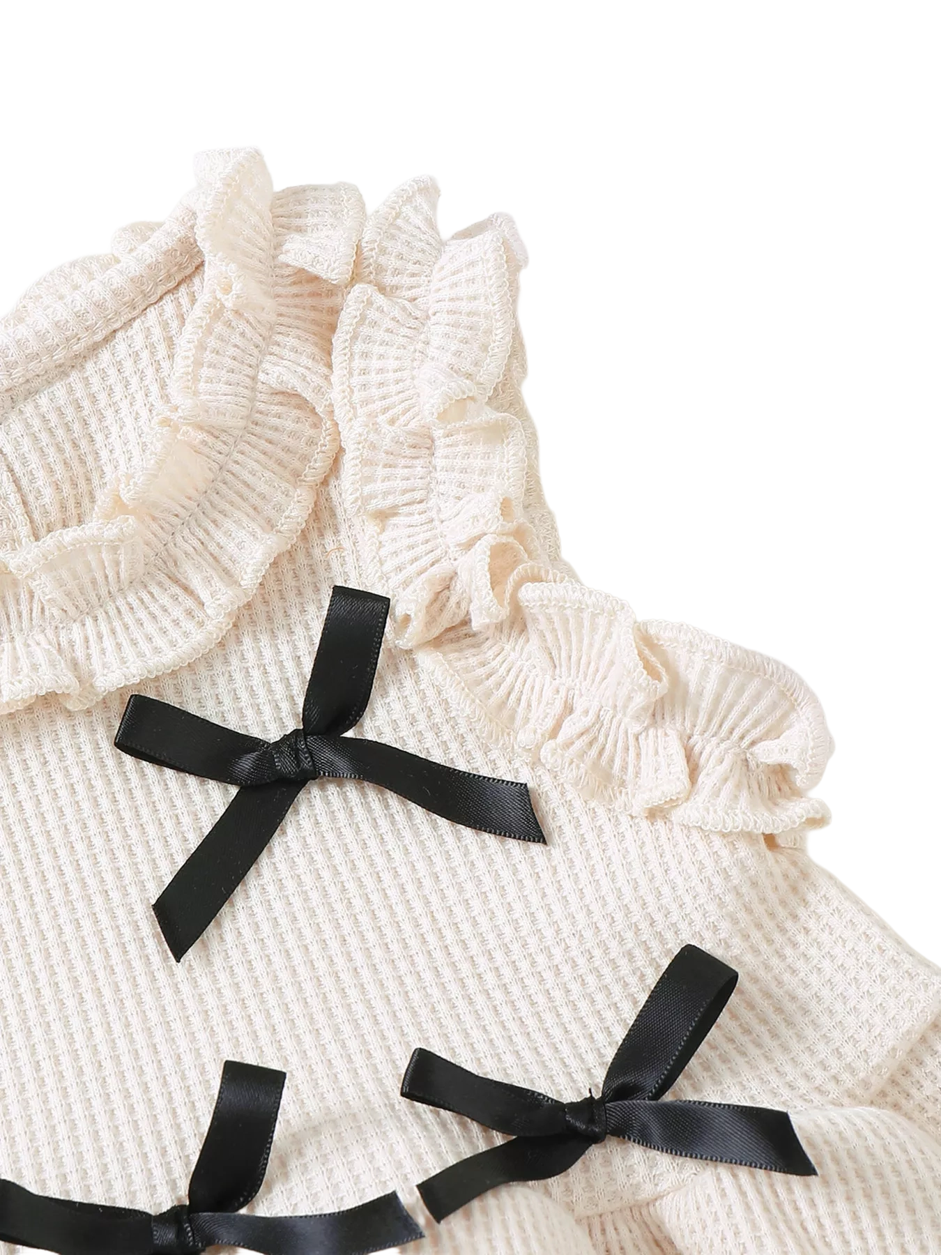 Ivory baby waffle knit top with black satin bows and layered ruffle shoulder trim, bodice close-up