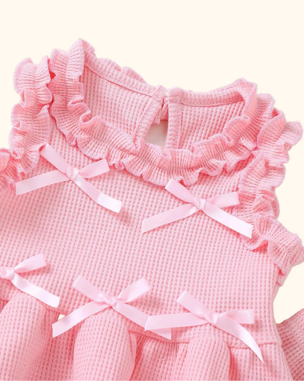 Pink baby waffle knit top with ruffled neckline, shoulder trim and pale pink bows, bodice close-up