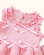 Pink baby waffle knit top with ruffled neckline, shoulder trim and pale pink bows, bodice close-up