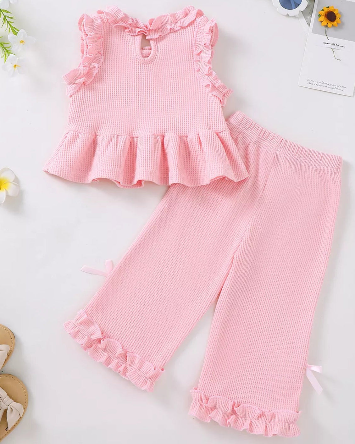 Pink baby waffle knit top and wide-leg pants set with ruffled hems and bow accents, flat lay view