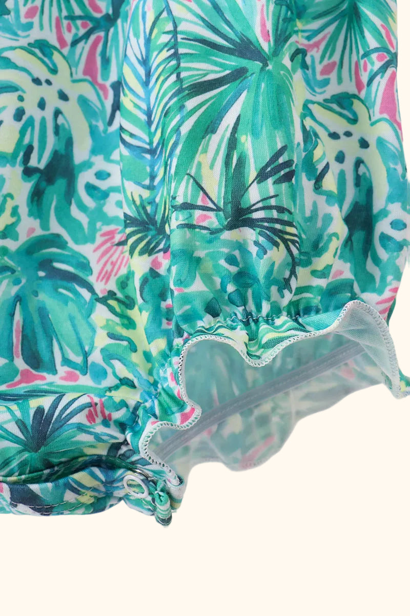 Green botanical baby romper with gathered leg opening and pink print accents, close-up view