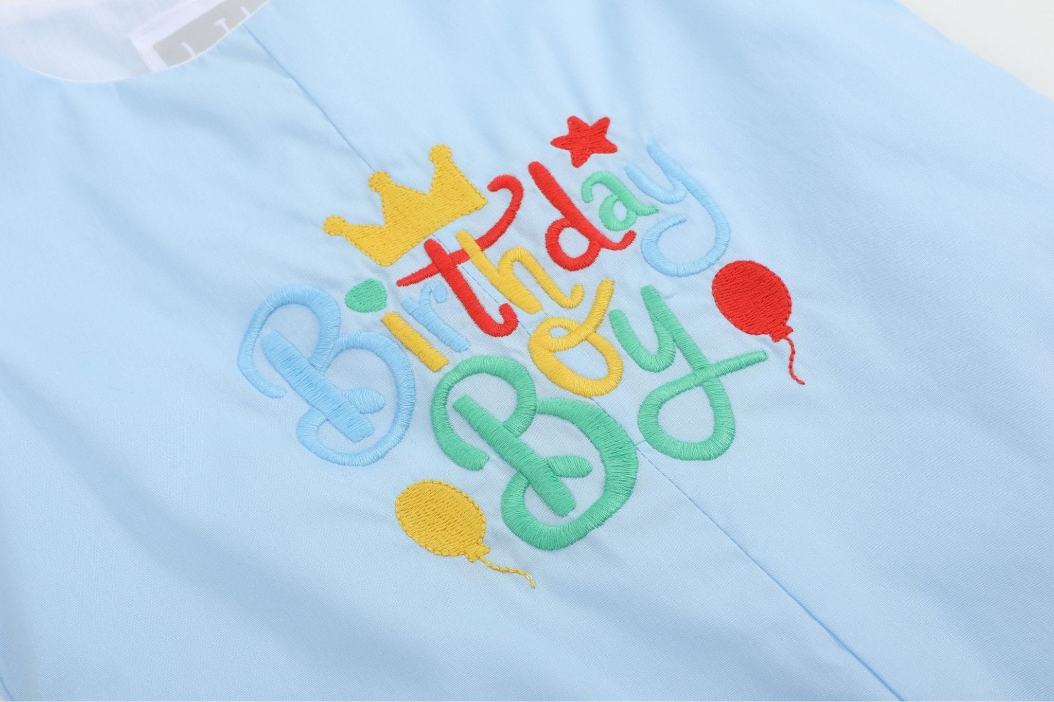 Light blue baby shortalls with colorful Birthday Boy embroidery, close-up view