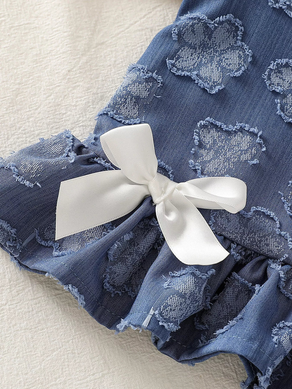 Blue baby flower tank with white bow and gathered ruffle hem, close-up detail view