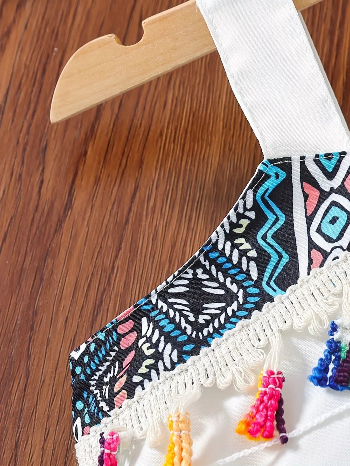 White kids tank with wide shoulder strap, geometric print and multicolor tassel trim, close-up view