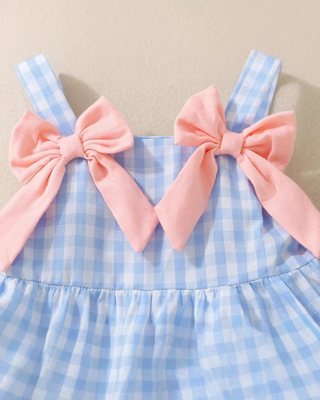 Blue gingham baby and toddler dress with oversized pink shoulder bows, upper front close-up