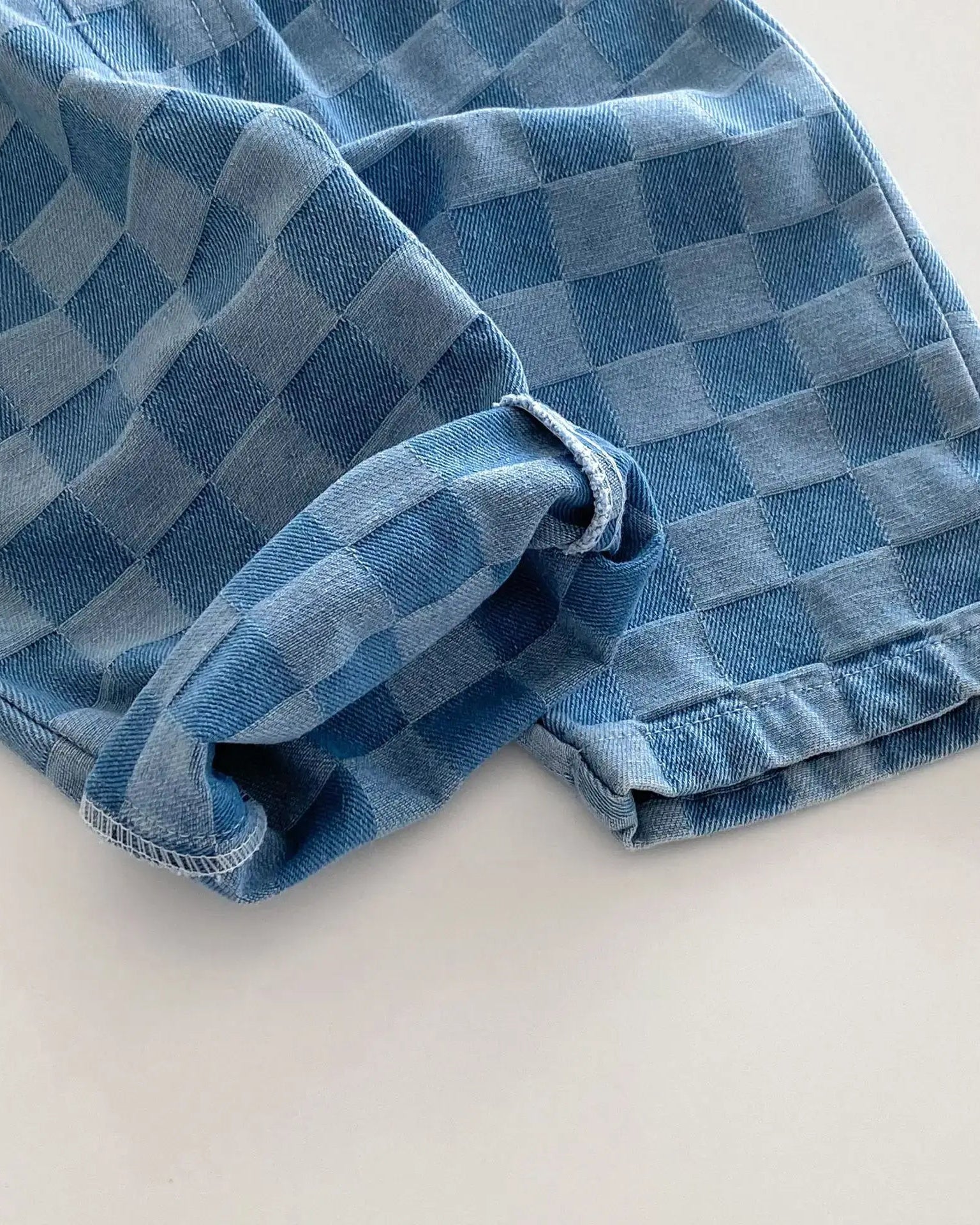 Blue plaid kids tapered trousers with rolled cuff and denim texture, close-up detail