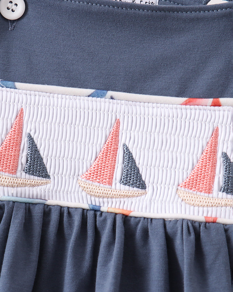 Blue smocked kids top with coral and navy embroidered sailboats, close-up view