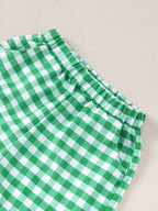 Green gingham baby shorts with elastic waistband and curved side pockets, close-up view