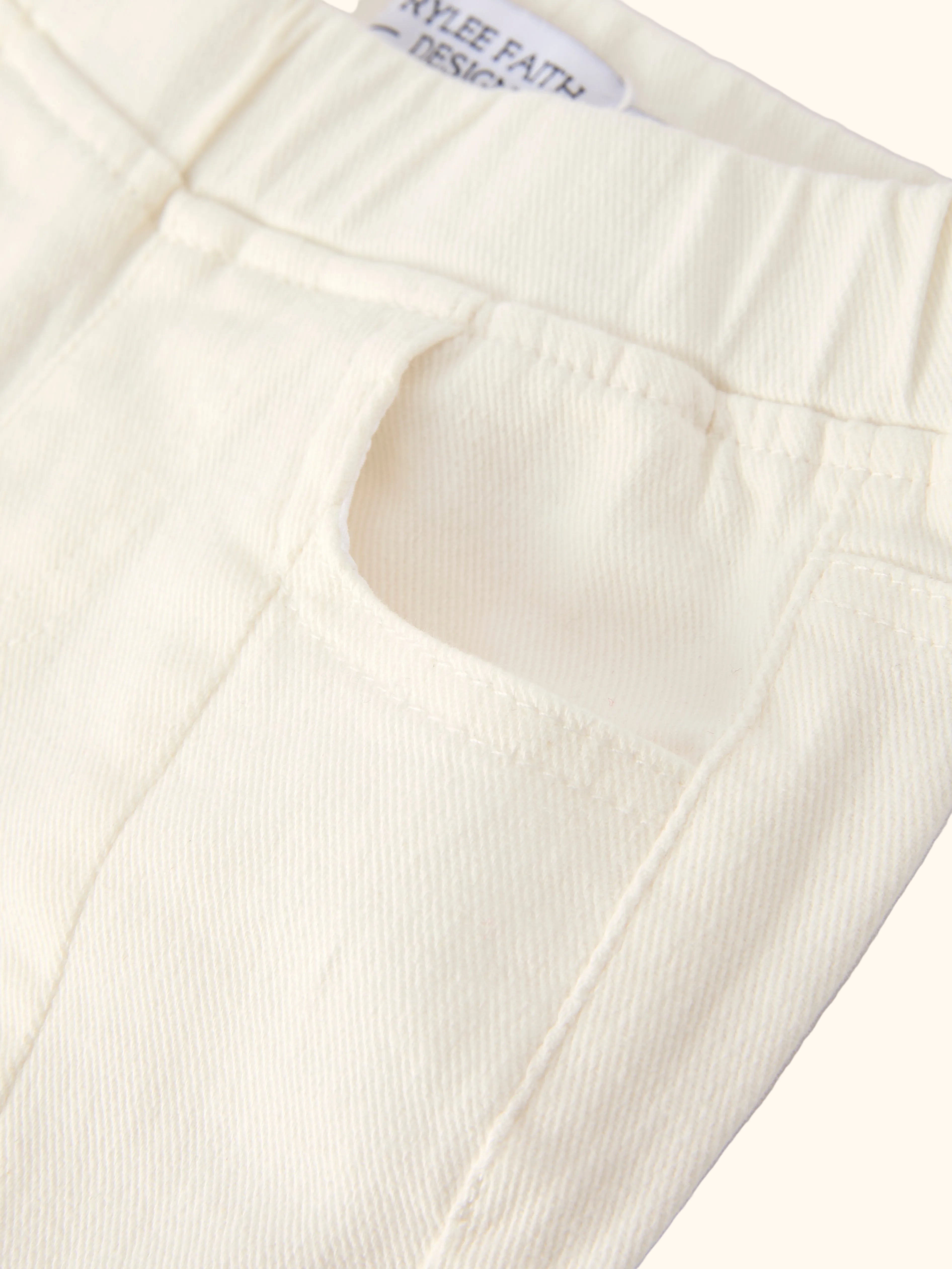 Ivory kids denim pants with elastic waistband, curved front pocket and front seam, close-up view