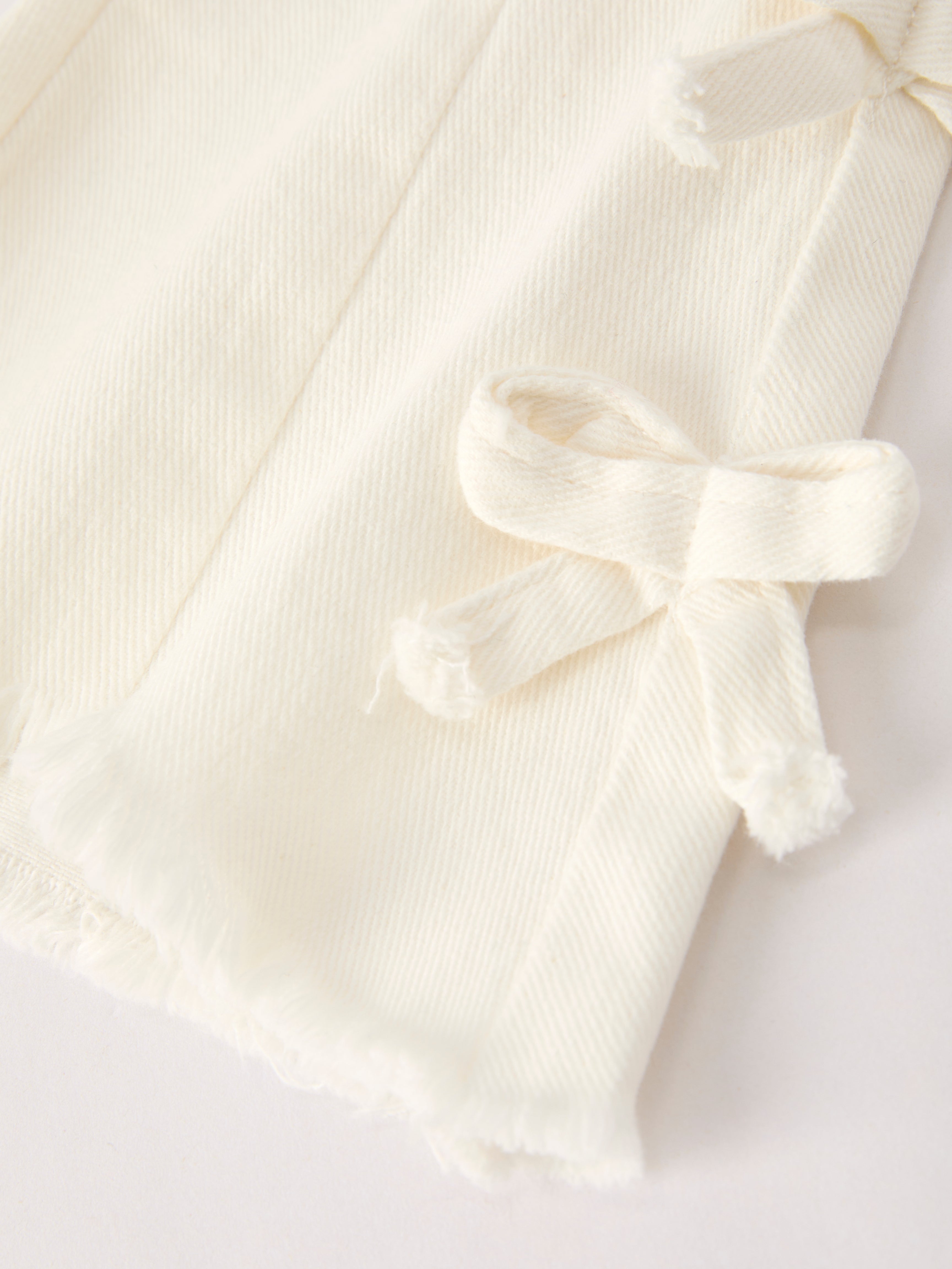Ivory kids flare denim pants with fabric bow details and frayed raw-edge hem, lower-leg close-up