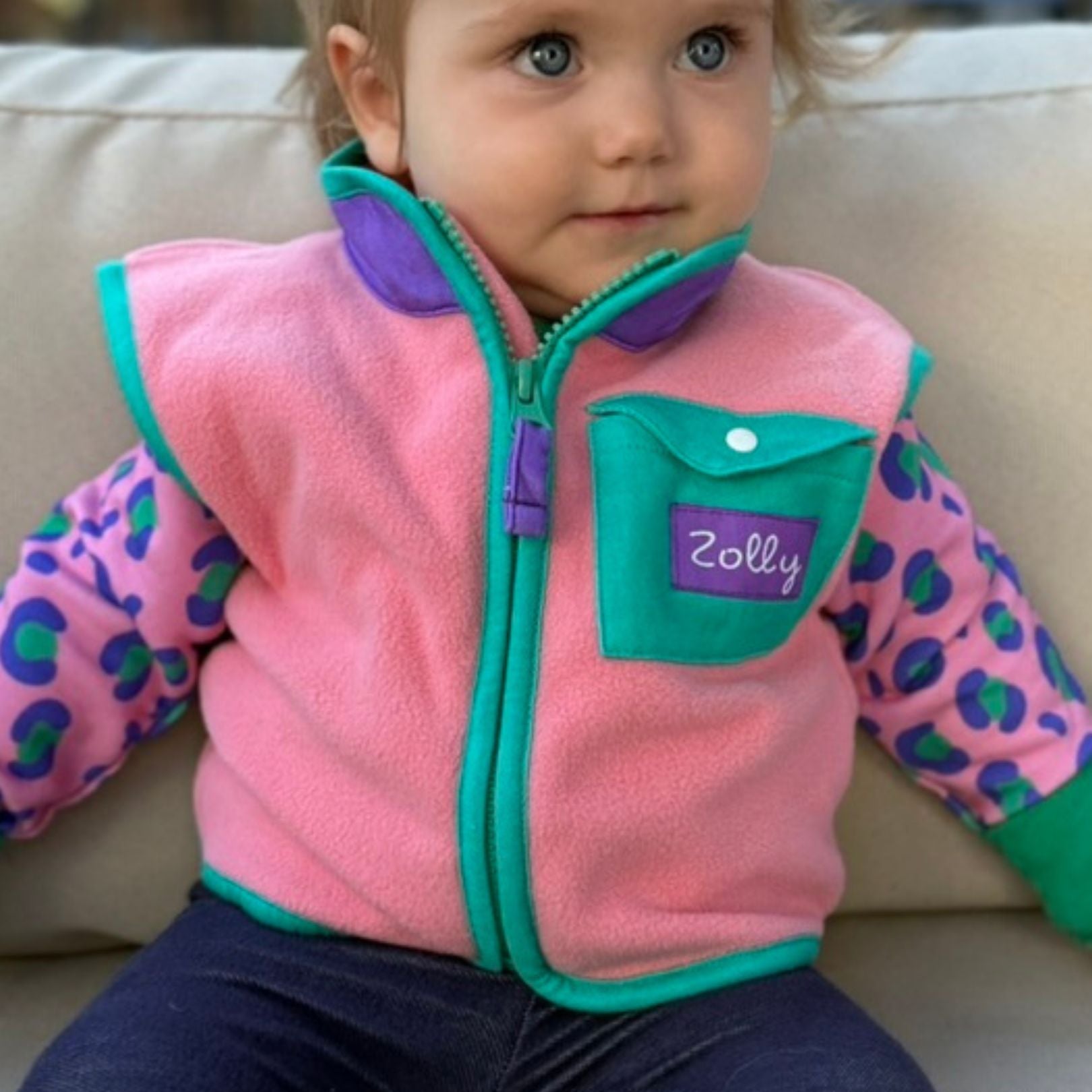 Bubblegum pink baby fleece vest with teal trim and snap chest pocket, modeled front view