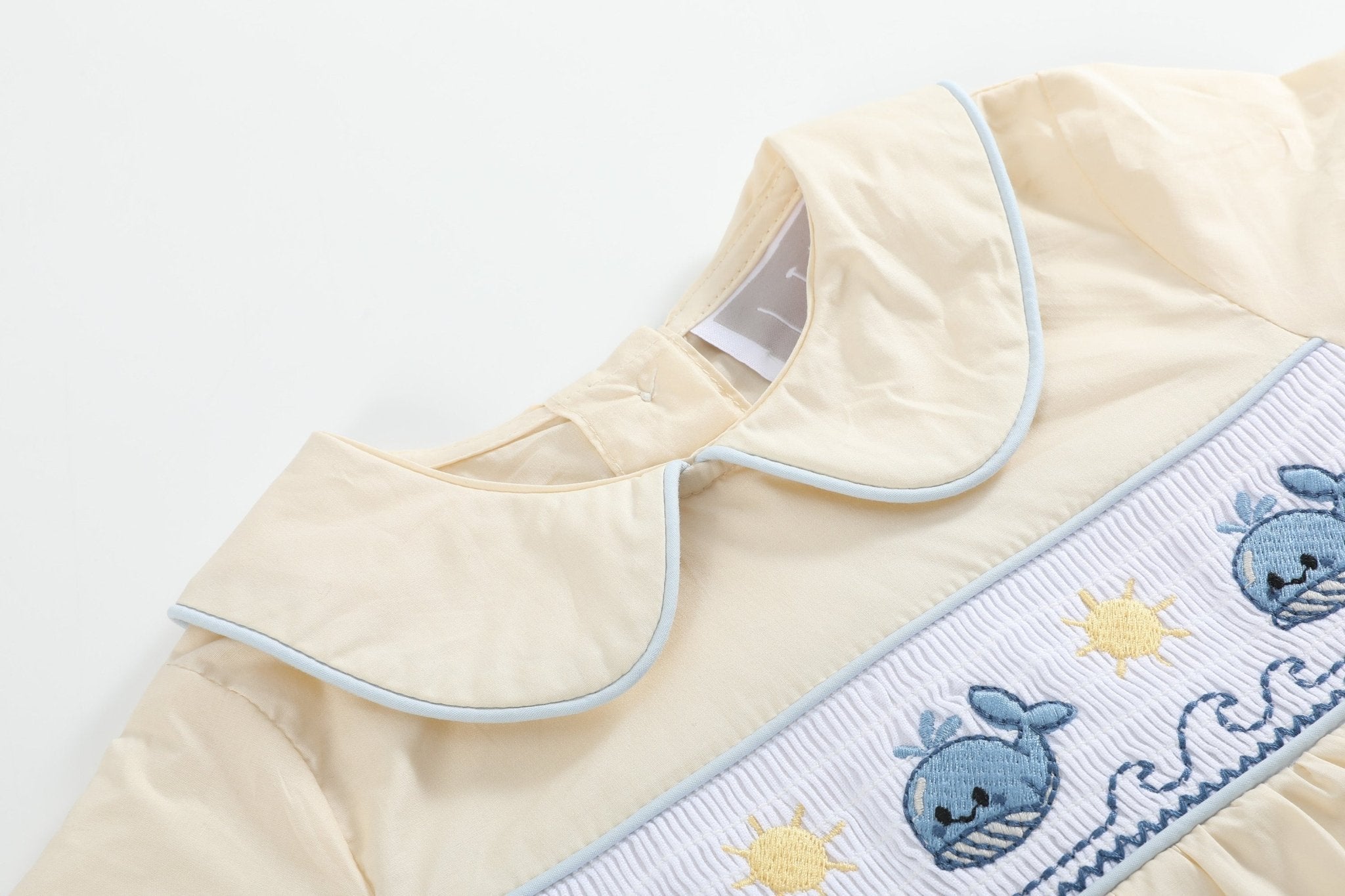 Buttercream yellow baby smocked romper with embroidered whales suns and waves, bodice close-up