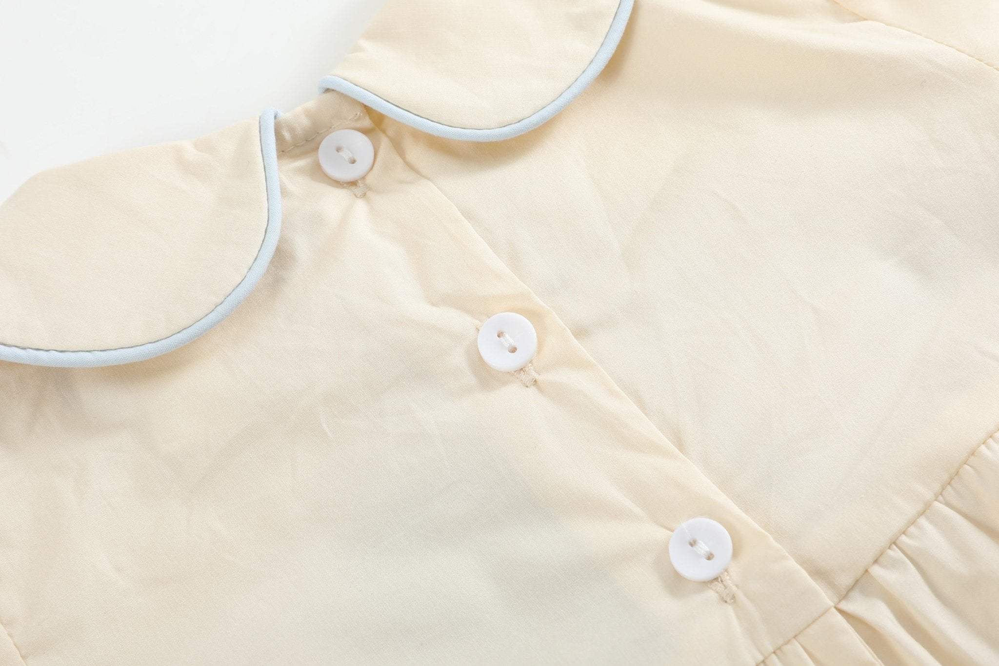 Buttercream yellow baby romper with blue-trimmed Peter Pan collar and back buttons, close-up view