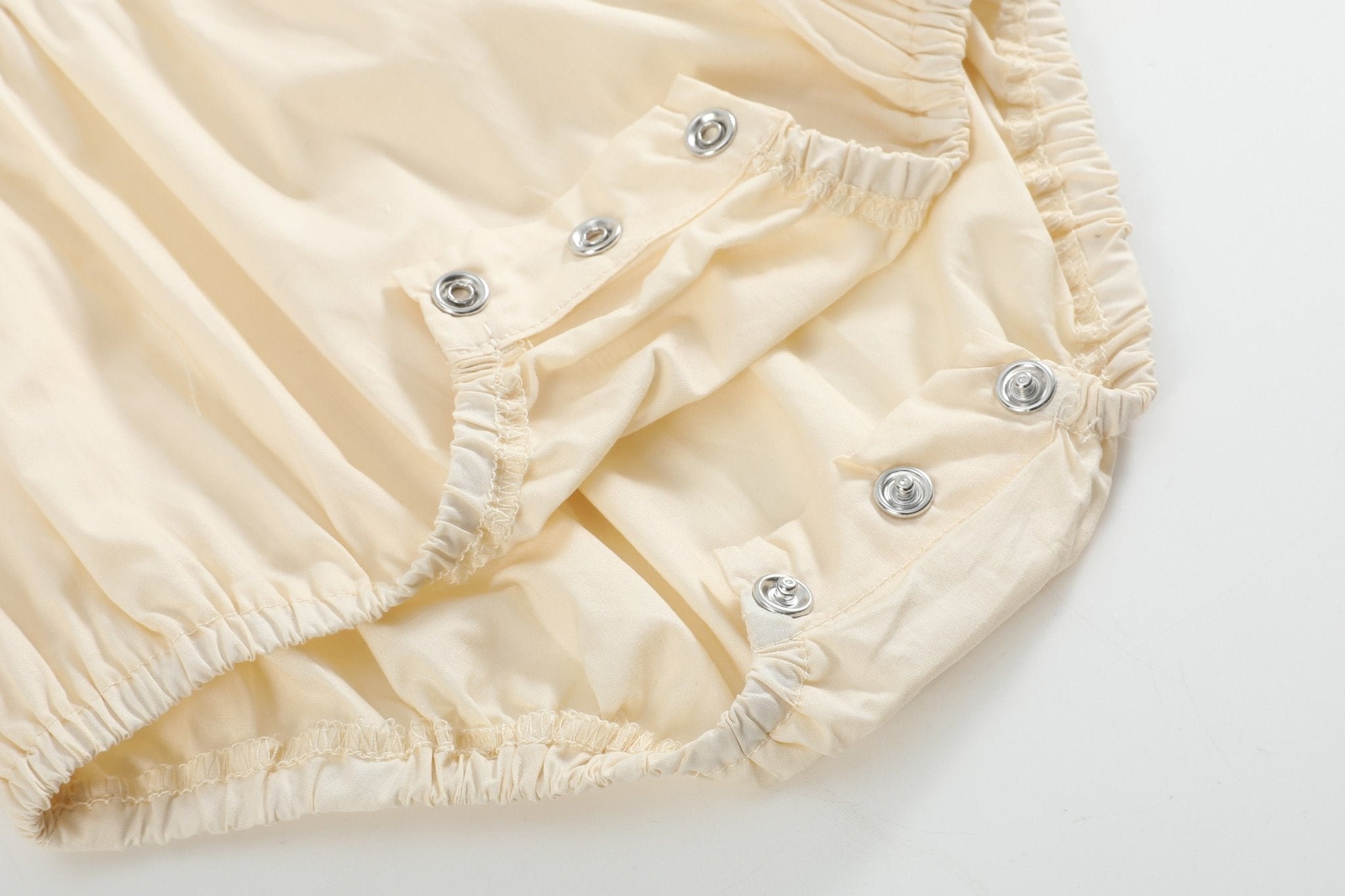 Buttercream yellow baby romper with bottom snaps and elasticized leg openings, close-up view