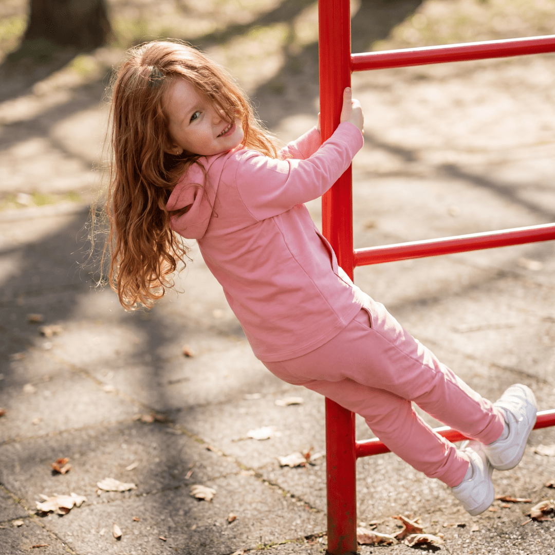 Carnation pink kids hooded jogger set with matching pants, playground side view