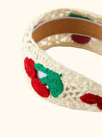 Cream kids headband with raised red cherry and green leaf crochet appliqué, design close-up