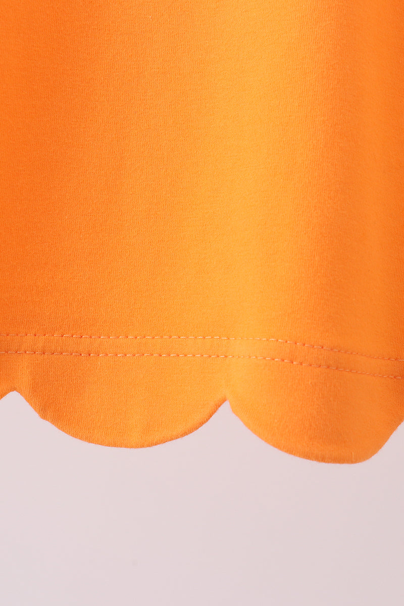 Orange kids top with rounded scalloped bottom hem, close-up detail view