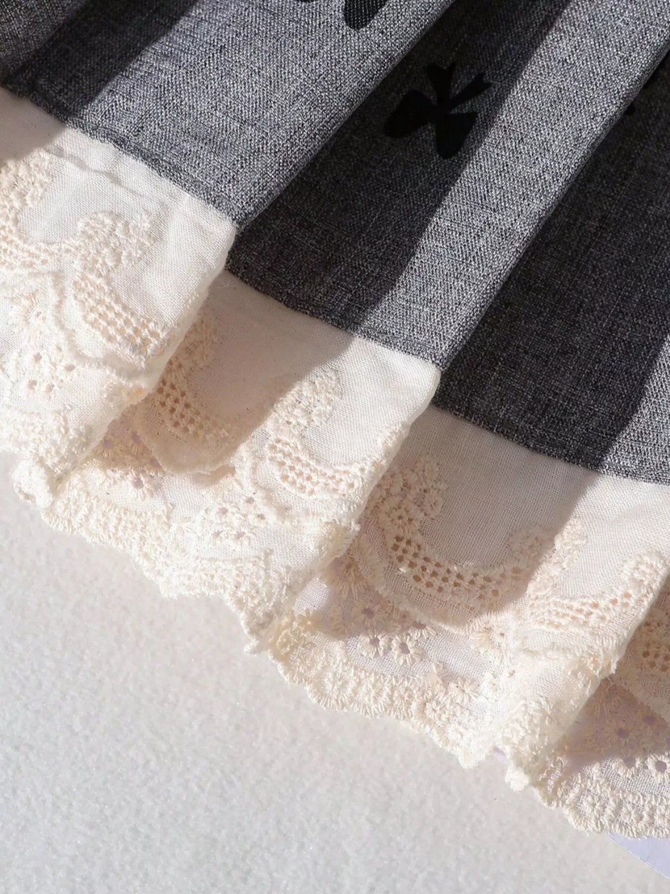 Grey kids bow print pleated skirt with ivory embroidered lace hem, hem close-up