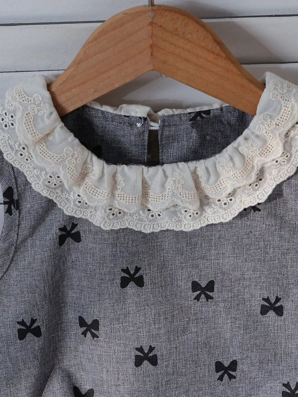 Grey kids bow print sleeveless top with ivory lace ruffle collar, neckline close-up