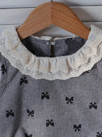 Grey kids bow print sleeveless top with ivory lace ruffle collar, neckline close-up