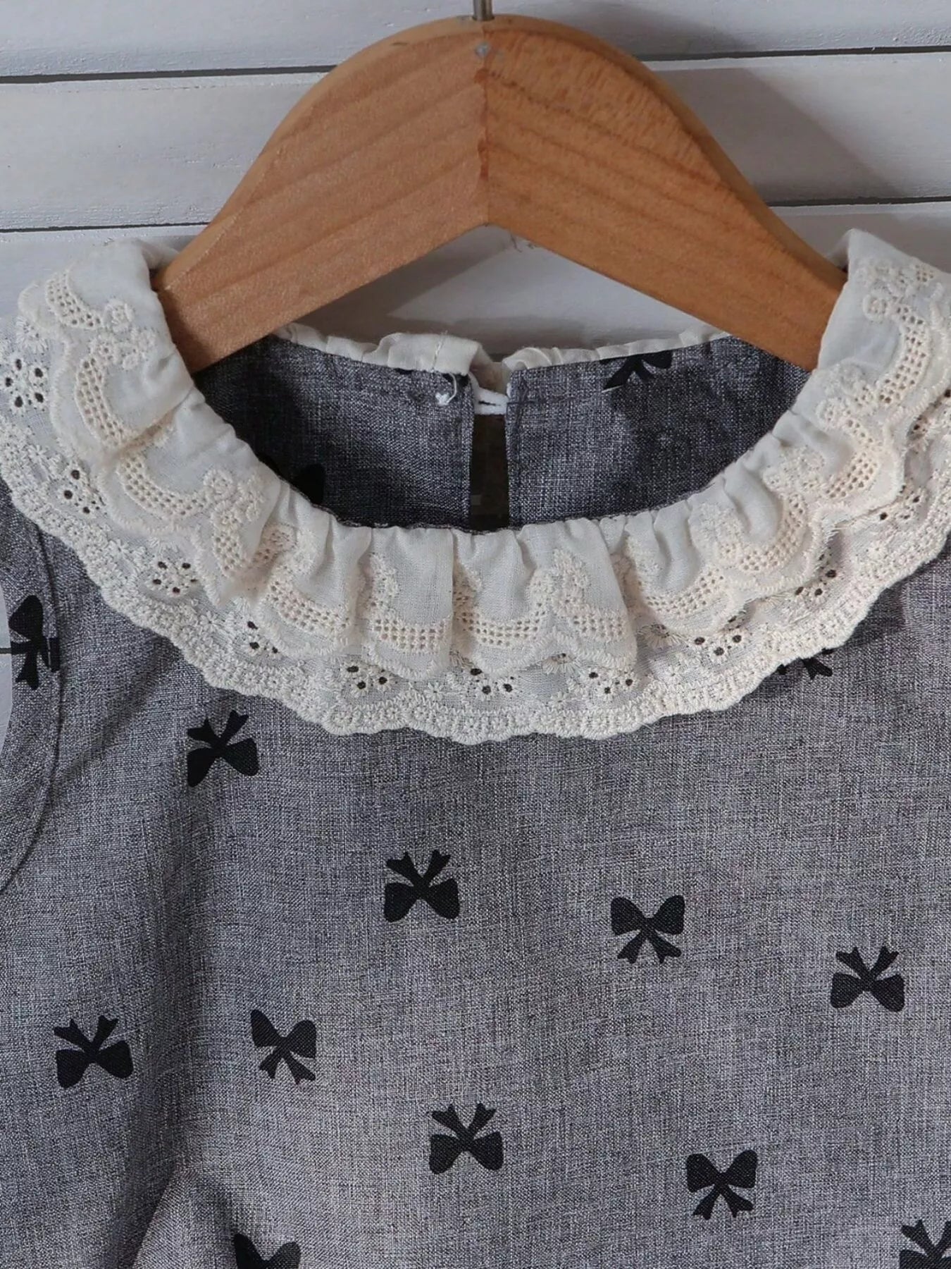 Grey kids bow print sleeveless top with ivory lace ruffle collar, neckline close-up