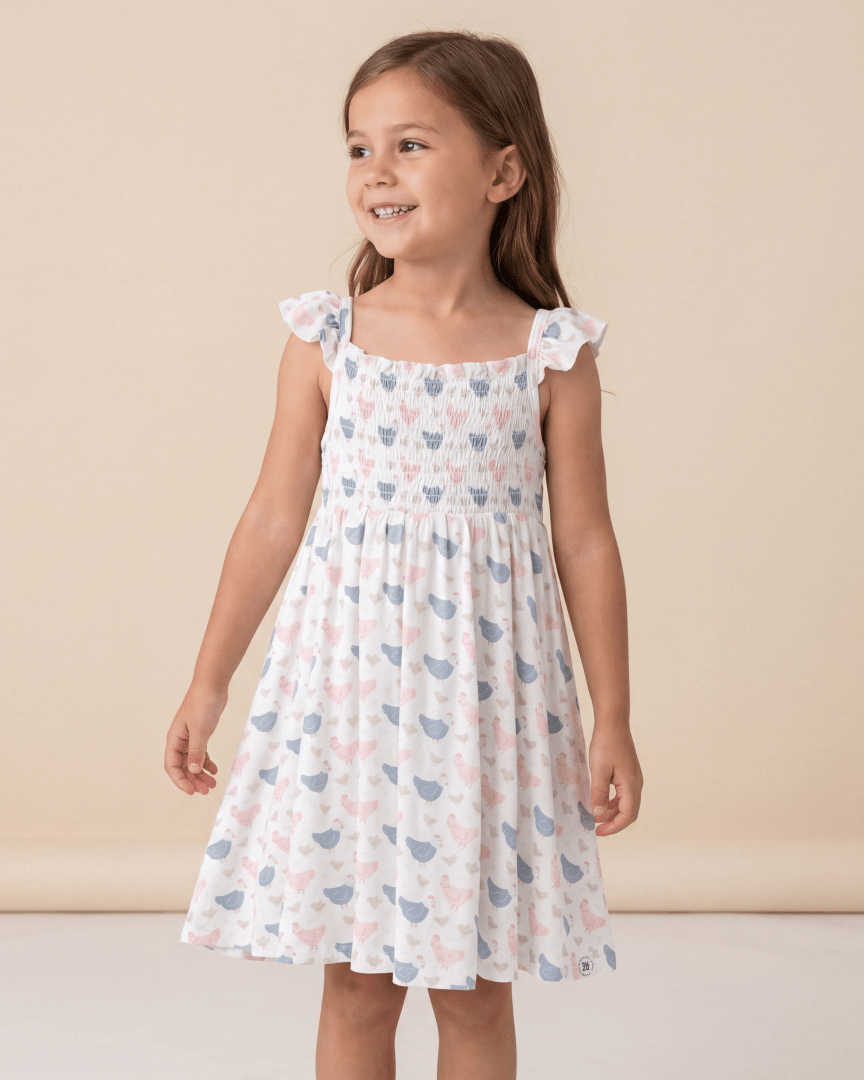 White kids bamboo smocked dress with pastel pink and blue hens, modeled front view