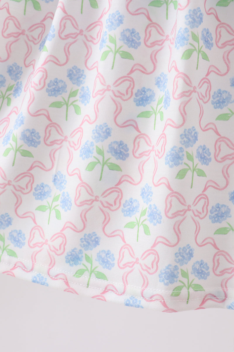 White kids dress with blue hydrangea flowers and pink bow print, fabric close-up view