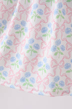 White kids dress with blue hydrangea flowers and pink bow print, fabric close-up view