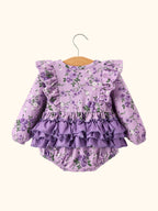 Lavender floral baby romper with layered purple back ruffles and long sleeves, back view