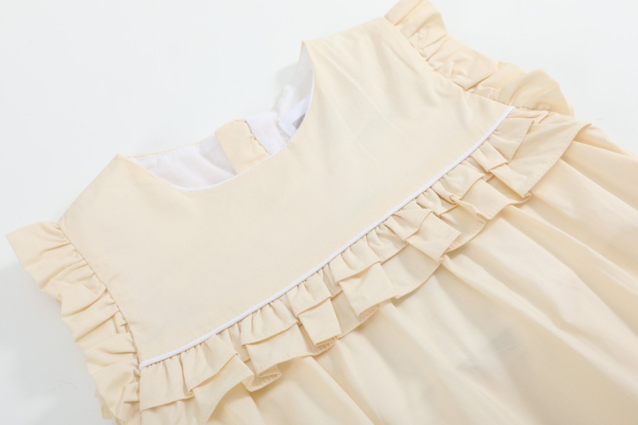 Light yellow baby romper with double-layer ruffle and white piping, bodice close-up