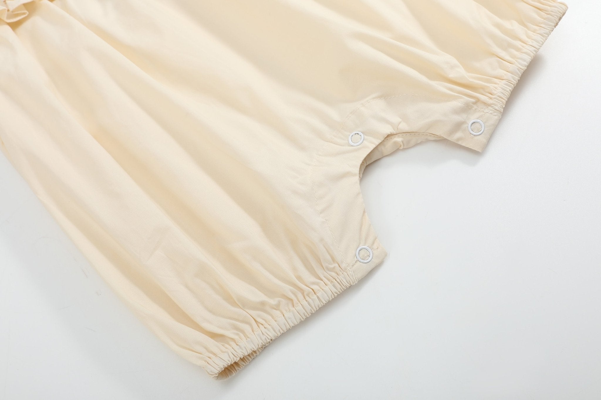 Light yellow baby romper with elasticized leg openings and three bottom snaps, close-up view
