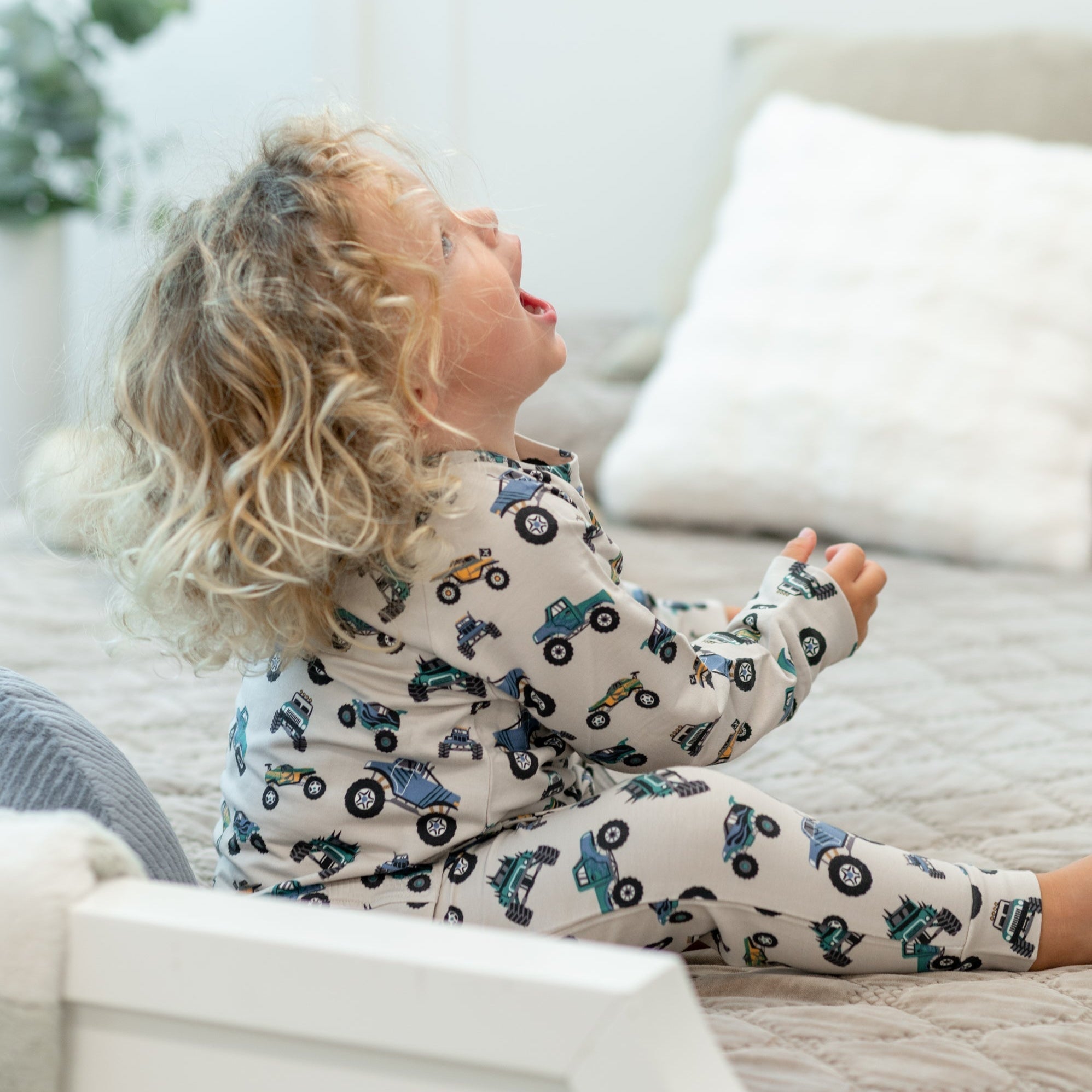 Ivory kids crew neck jogger set with blue and green truck print, seated side lifestyle view