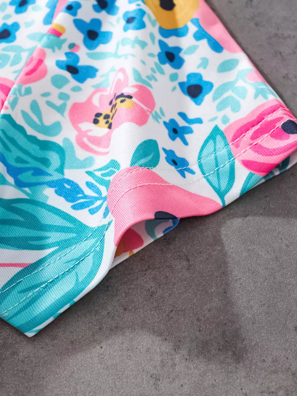 Multicolor kids floral print fabric with aqua leaves and pink flowers, stitching close-up