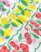 White kids dress fabric with yellow lemons, red cherries, green leaves and pink flowers, print close-up