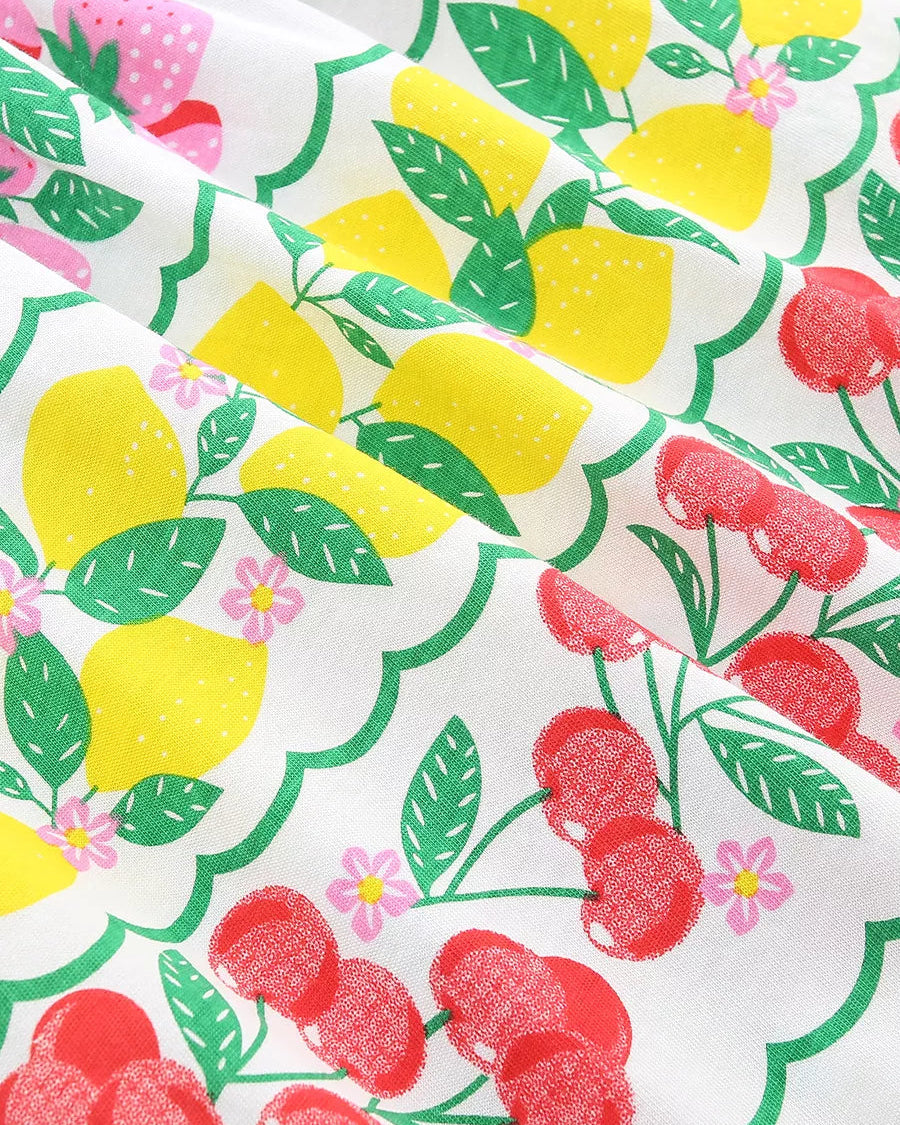 White kids dress fabric with yellow lemons, red cherries, green leaves and pink flowers, print close-up