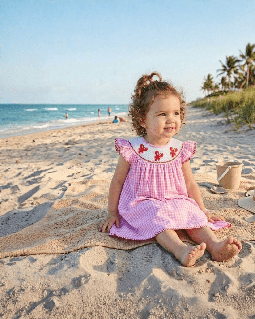 Pink gingham crawfish smocked bishop dress with ruffle sleeves, modeled beach view
