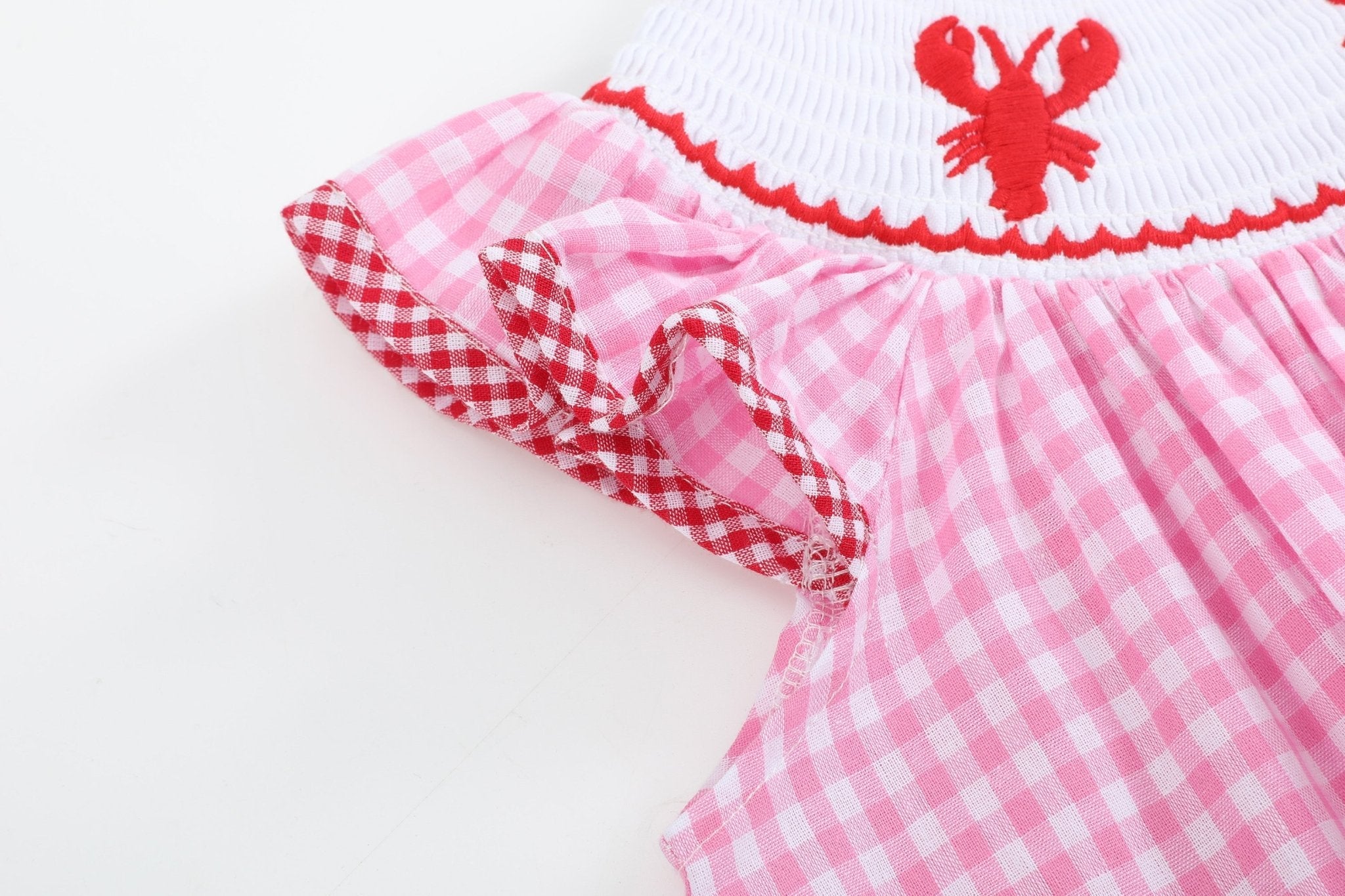 Pink gingham kids bishop dress with ruffle sleeve and red gingham trim, close-up view
