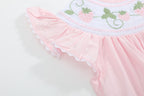 Pink baby strawberry romper with flutter sleeve and white scalloped trim, close-up view