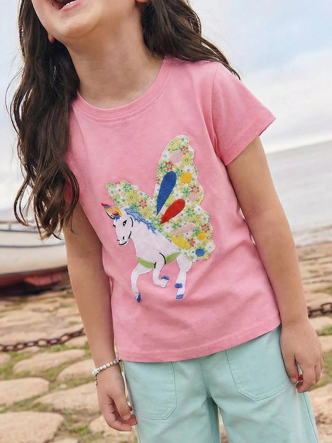 Pink kids winged unicorn appliqué T-shirt worn by child, front lifestyle view