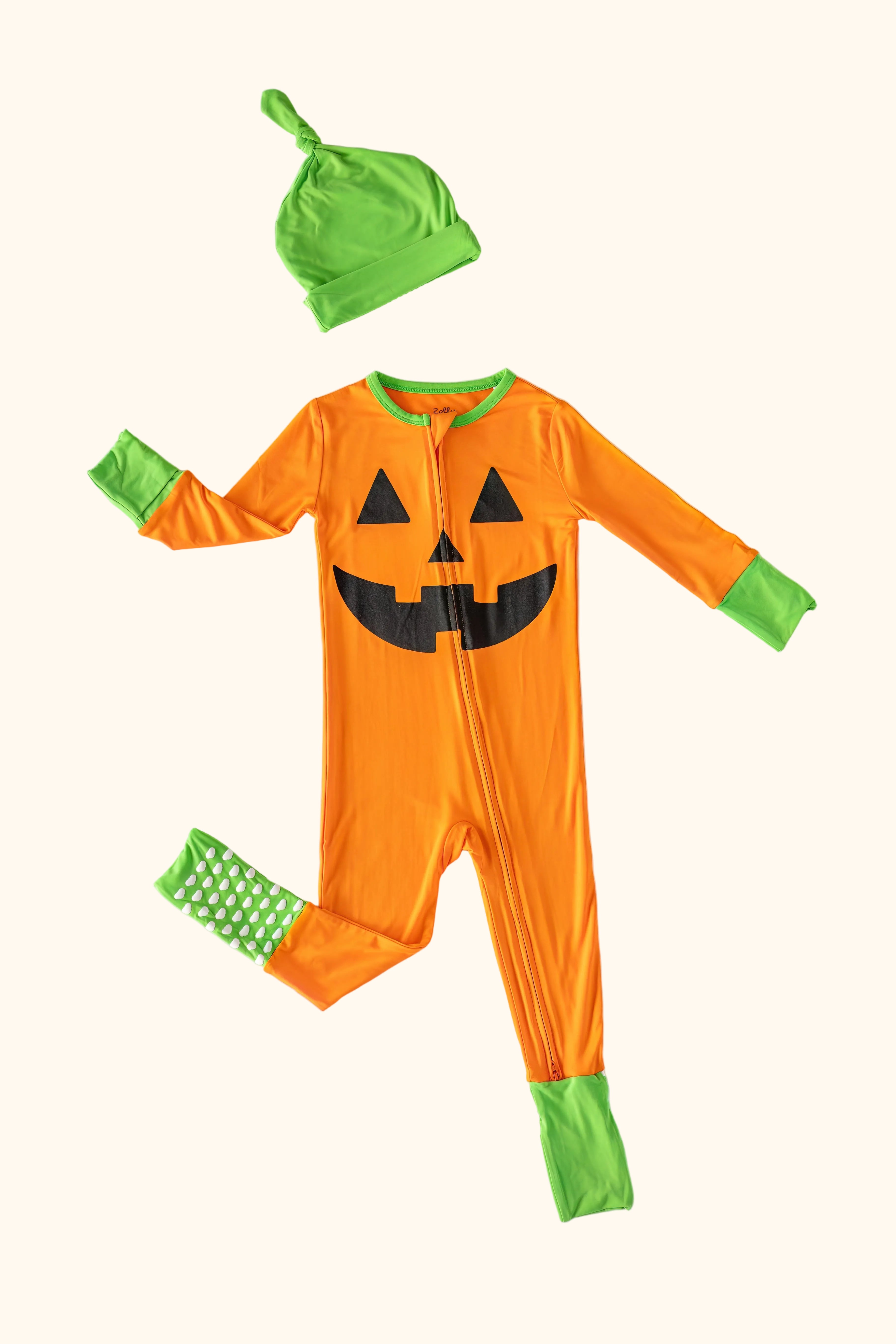 Orange baby jack-o’-lantern zipper pajama with matching green hat and fold-over cuffs, flat-lay view