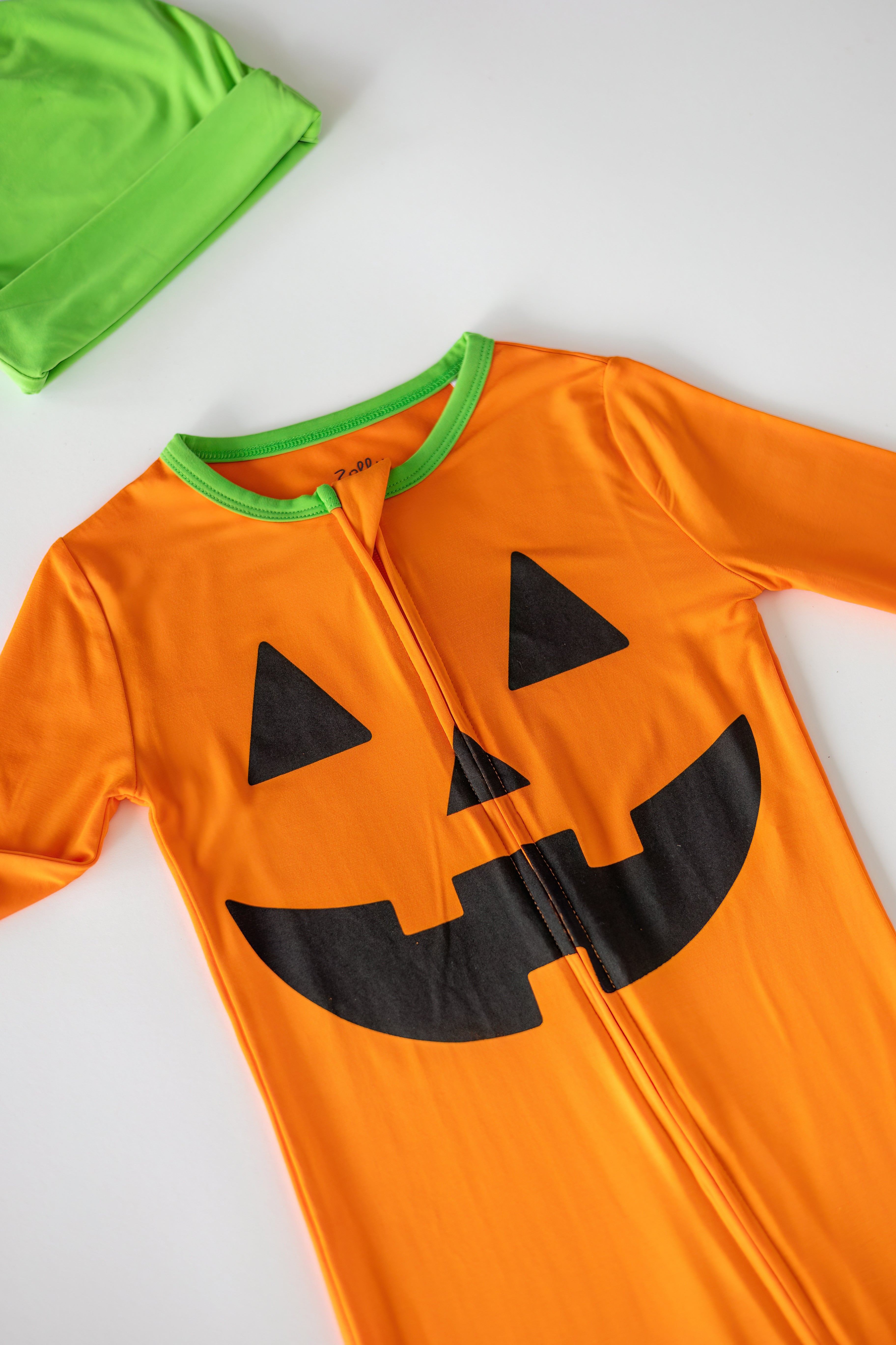Orange pumpkin bamboo pajama with black jack-o’-lantern graphic and green neckline, front detail view