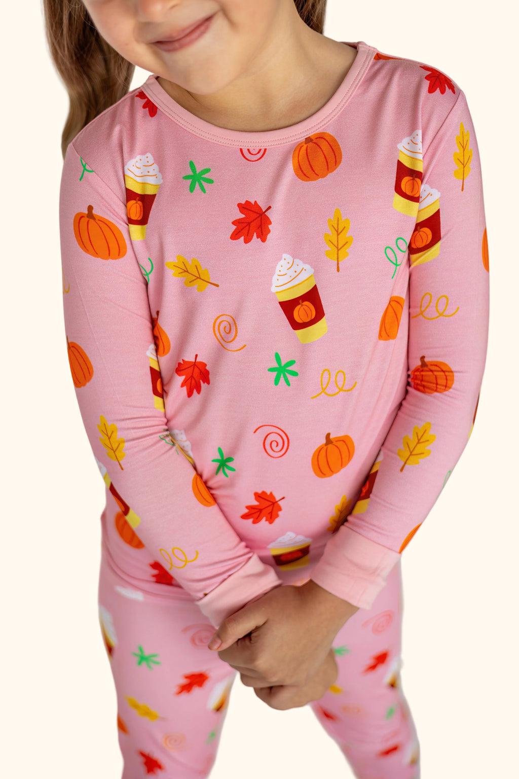 Pink kids Pumpkin Spice bamboo pajama set with pumpkins leaves and drink cups, modeled close-up view