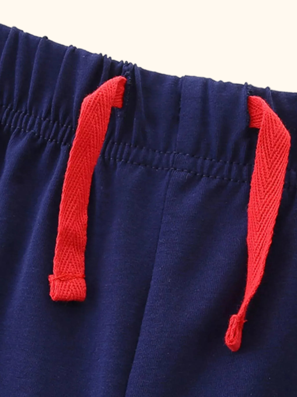 Navy kids shorts with elastic waistband and red tie detail, close-up view