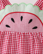 Red gingham watermelon dress with embroidered seed details and green scalloped trim, close-up view