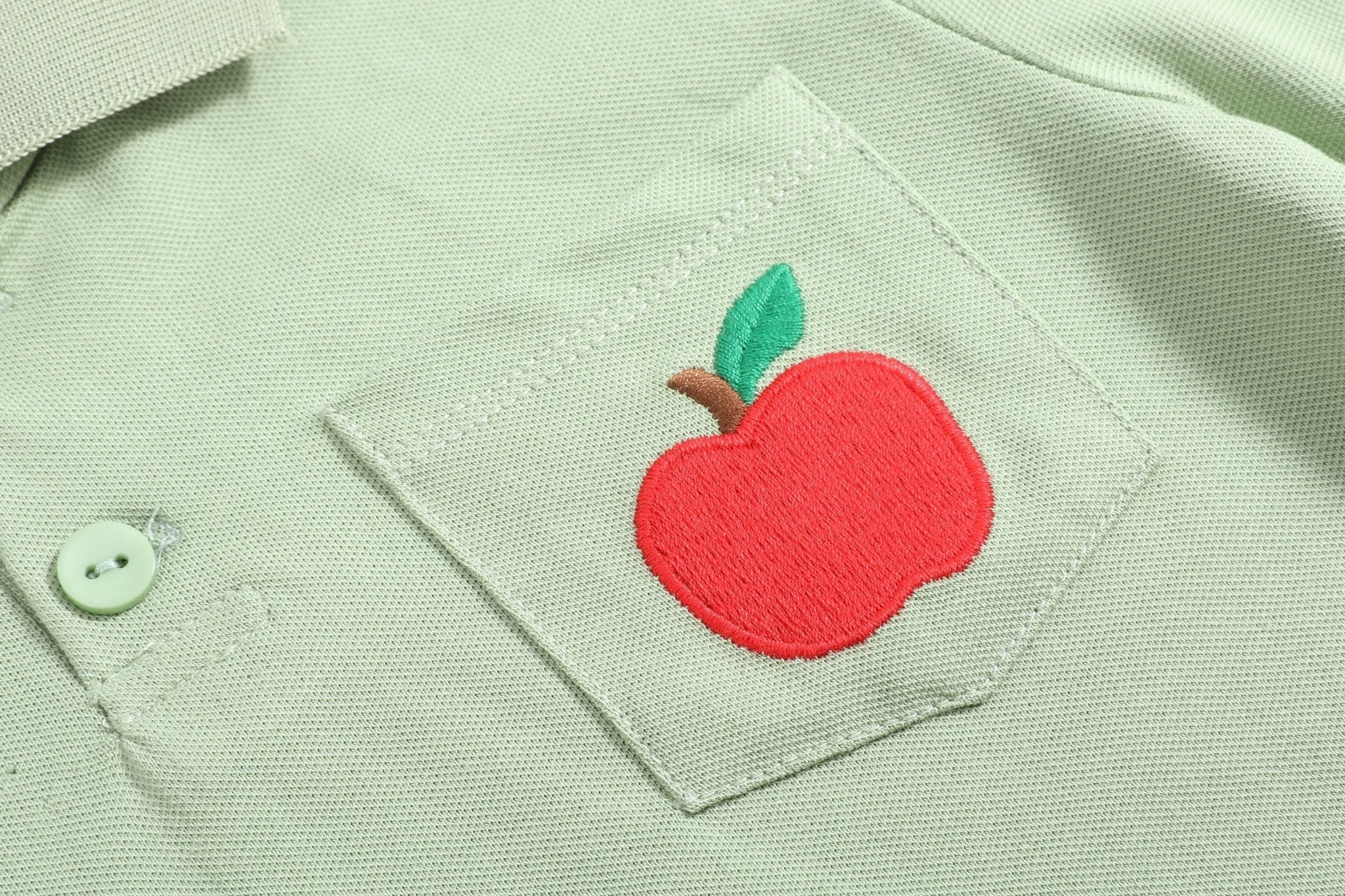 Sage green kids polo shirt with embroidered red apple on chest pocket, embroidery close-up